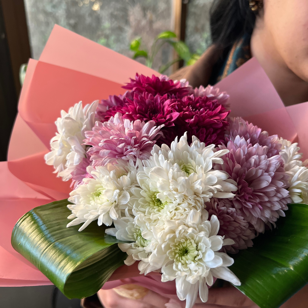 Bouquet of white and pink flowers with green leaves on a pink paper wrap.