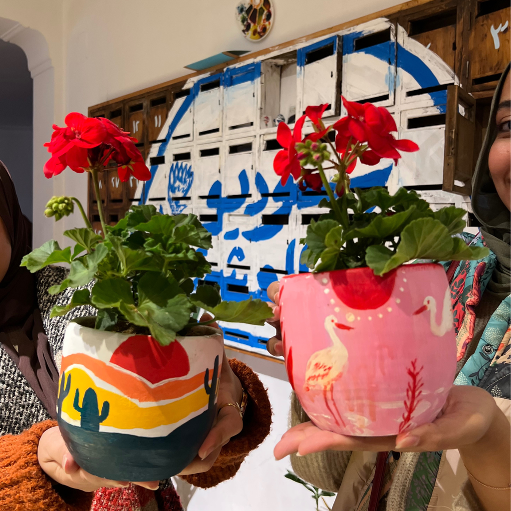 Two customized and painted plant pots with a red flower planted in them. 